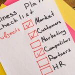 A handwritten business plan checklist on a table with colorful papers indicating important topics for startups.